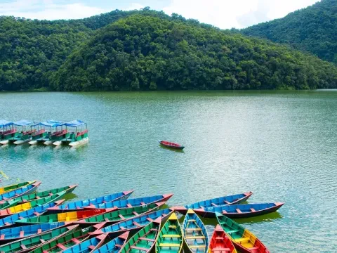 Colorful boats on Phewa Lake surrounded by scenic hills in Pokhara, Nepal.