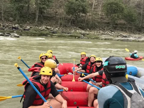 Adventure seekers enjoying white-water rafting on the Trishuli River in Nepal, surrounded by green hills and rocky riverbanks.