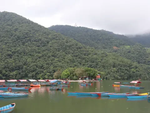 Beautiful Phewa Lake in Pokhara, Nepal, with colourful boats, green hills, and the Annapurna Himalayan mountain range.