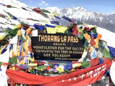 Thorong La Pass on the Annapurna Circuit Trek with trekkers and snow-covered Himalayan mountains in Nepal.