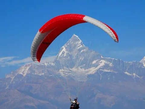 Tandem paraglider soaring above Pokhara with magnificent views of Mount Fishtail and the Annapurna Himalayan range, Nepal.