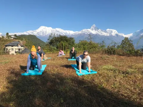 ravelers practicing yoga outdoors in Pokhara with panoramic views of the snow-covered Annapurna and Machhapuchhre mountain ranges in Nepal