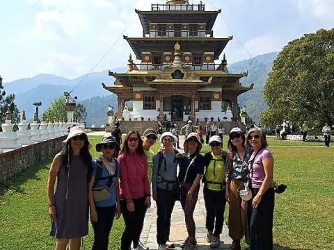 Travelers posing in front of a traditional Buddhist chorten surrounded by Himalayan hills in Bhutan.