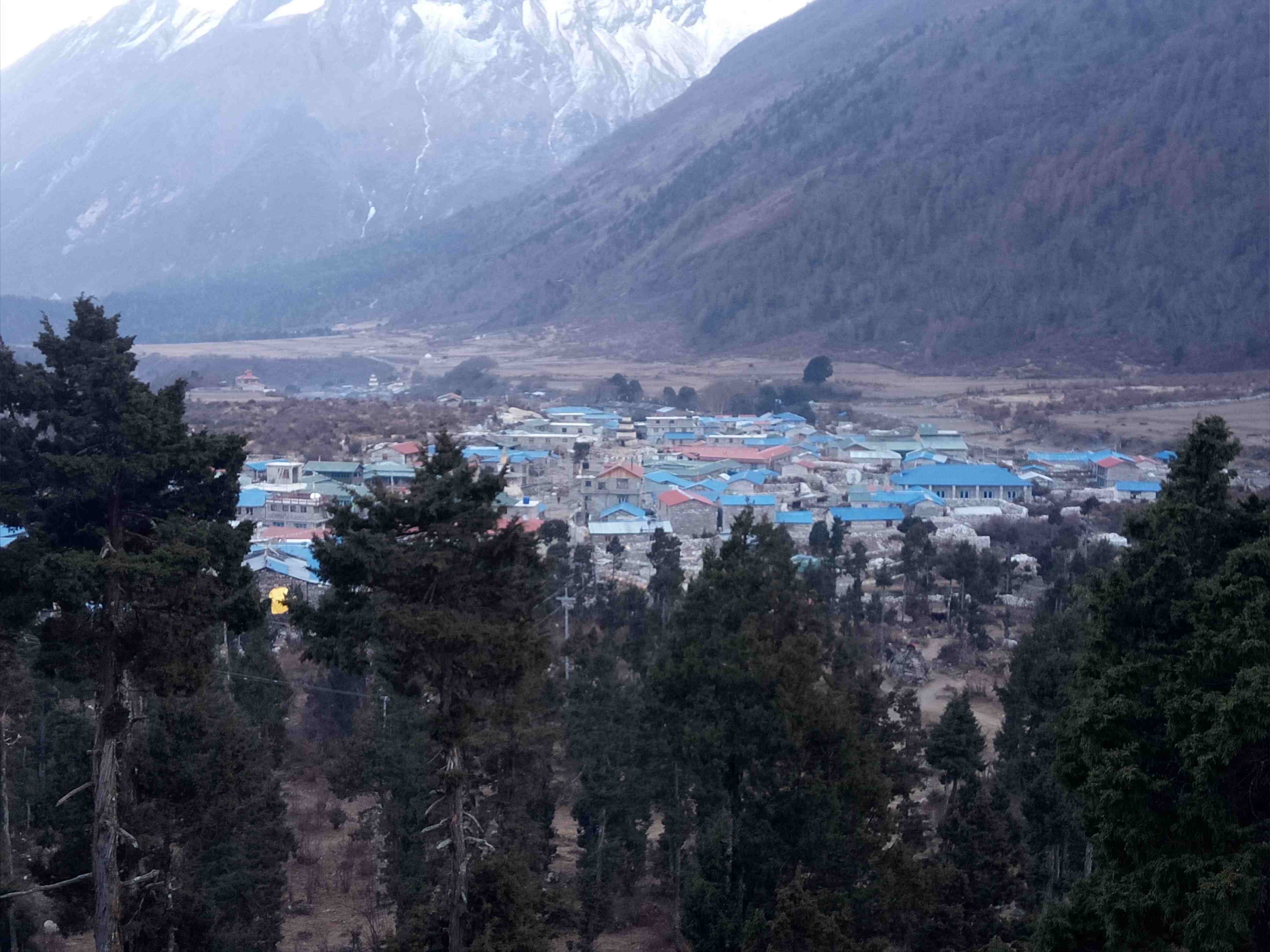 Samagaon village with traditional Tibetan-style stone houses, colorful prayer flags, grazing yaks, and the majestic Mt. Manaslu rising in the background under a crystal-clear October sky on the Manaslu Circuit Trek.