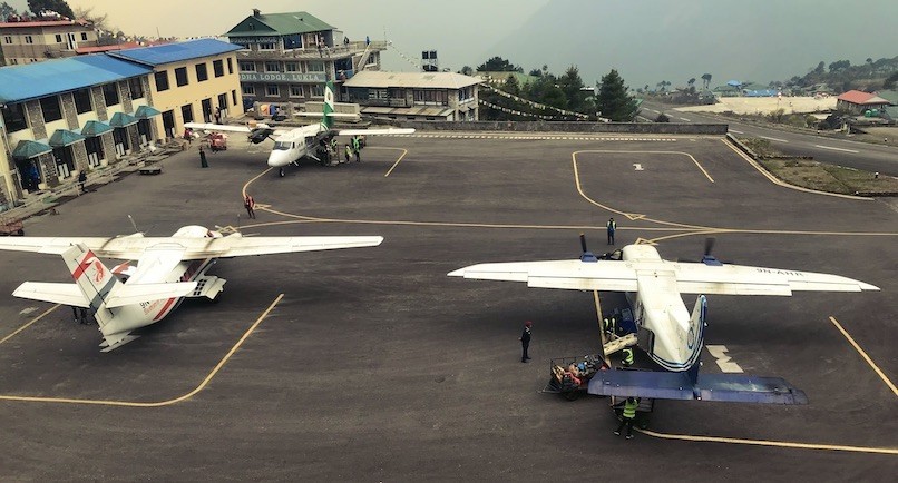 Twin Otter aircraft parked at Lukla Airport with helicopters and the famous mountain runway, serving as the main gateway to the Everest Base Camp Trek in Nepal.