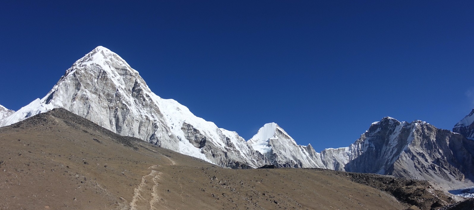 Rocky trail leading to Kala Patthar with trekkers, snow-covered Himalayan peaks, and clear mountain skies in the Everest region of Nepal.