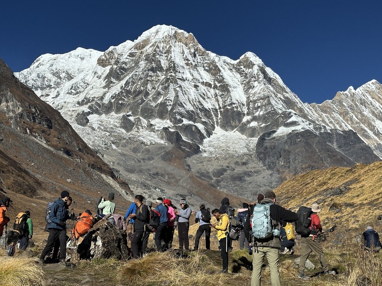 Crowded Annapurna Base Camp trail in October with trekkers hiking beneath towering snow-covered Himalayan peaks.