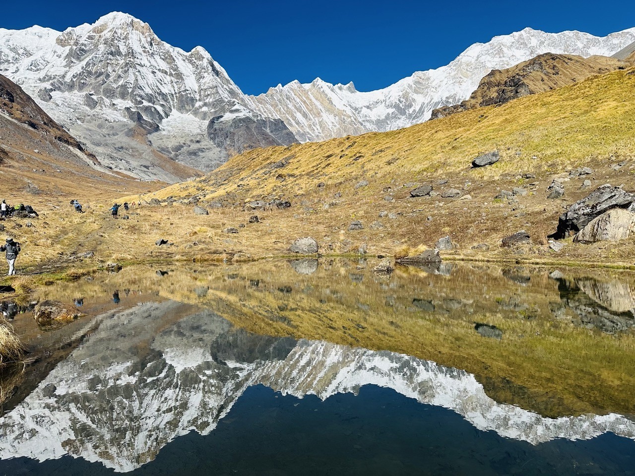 Snow-capped Himalayan mountains reflected in a calm alpine lake along the trekking route to Annapurna Base Camp in Nepal.