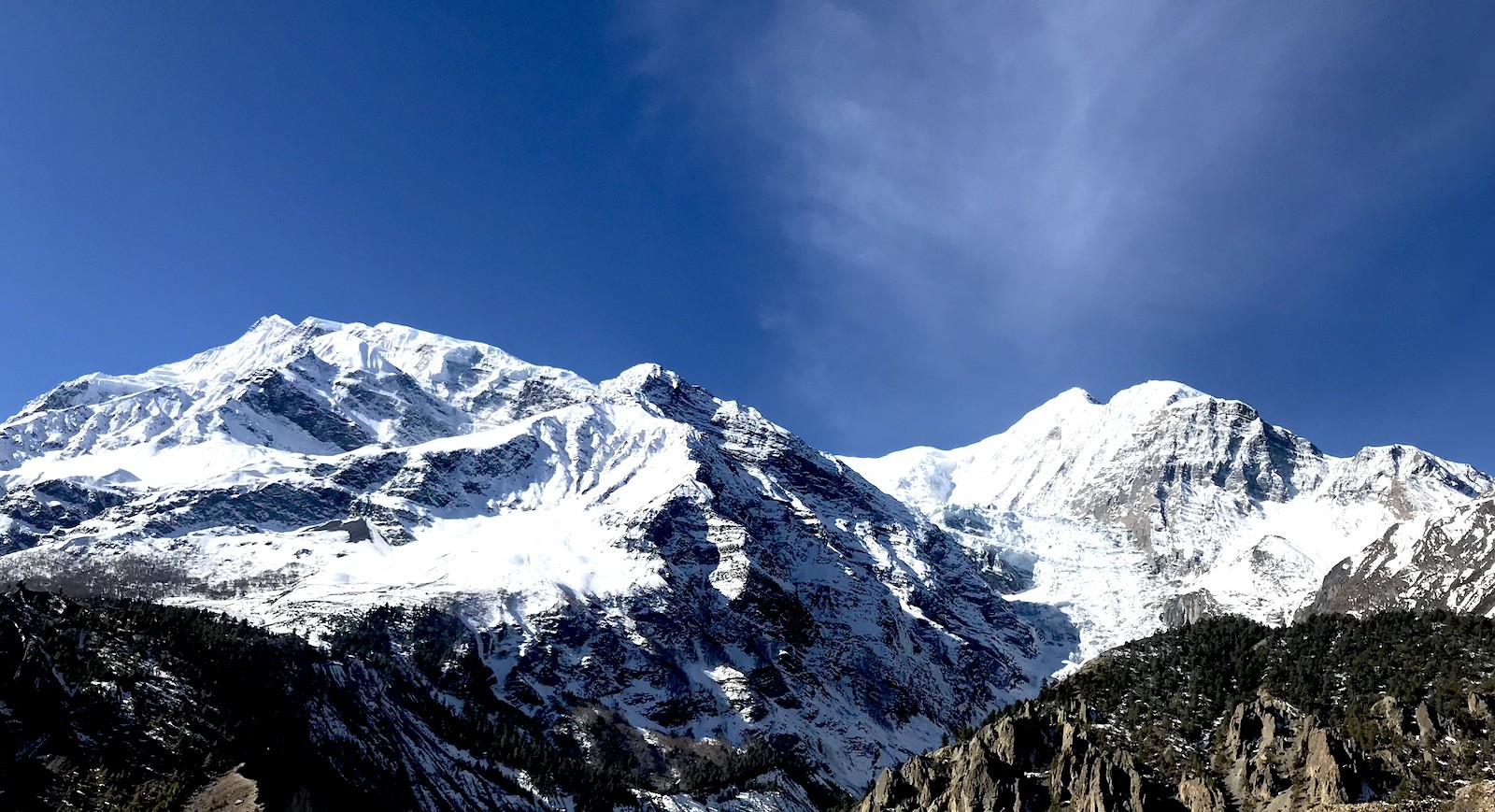 "Trekkers on the Annapurna Circuit enjoying crystal-clear views of snow-capped Himalayan peaks under a bright blue sky during the autumn trekking season in Nepal."