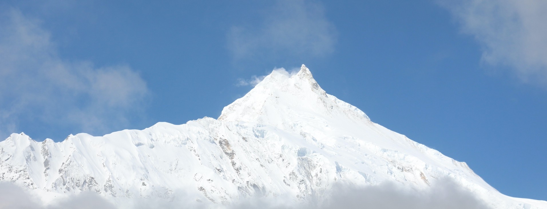 Mount Manaslu (8,163 m) rises majestically under a deep blue September sky, its snow-covered summit and glaciated ridges illuminated by bright sunshine on the Manaslu Circuit Trek