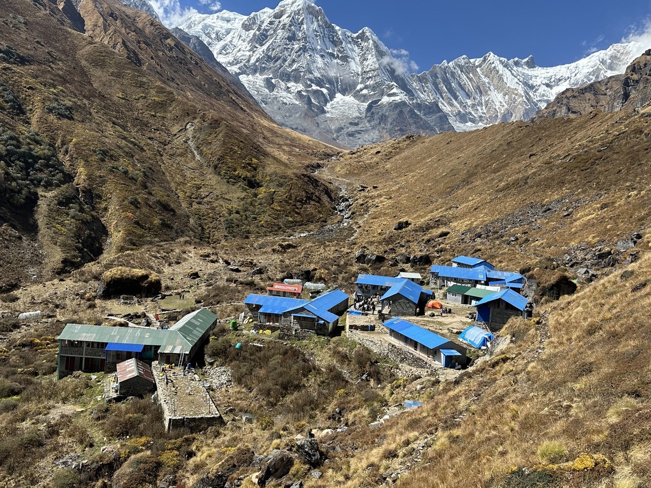 Machhapuchhre Base Camp (MBC) lodges beside a clear trekking trail, surrounded by dramatic Himalayan peaks and pristine alpine landscapes under a bright mountain sky