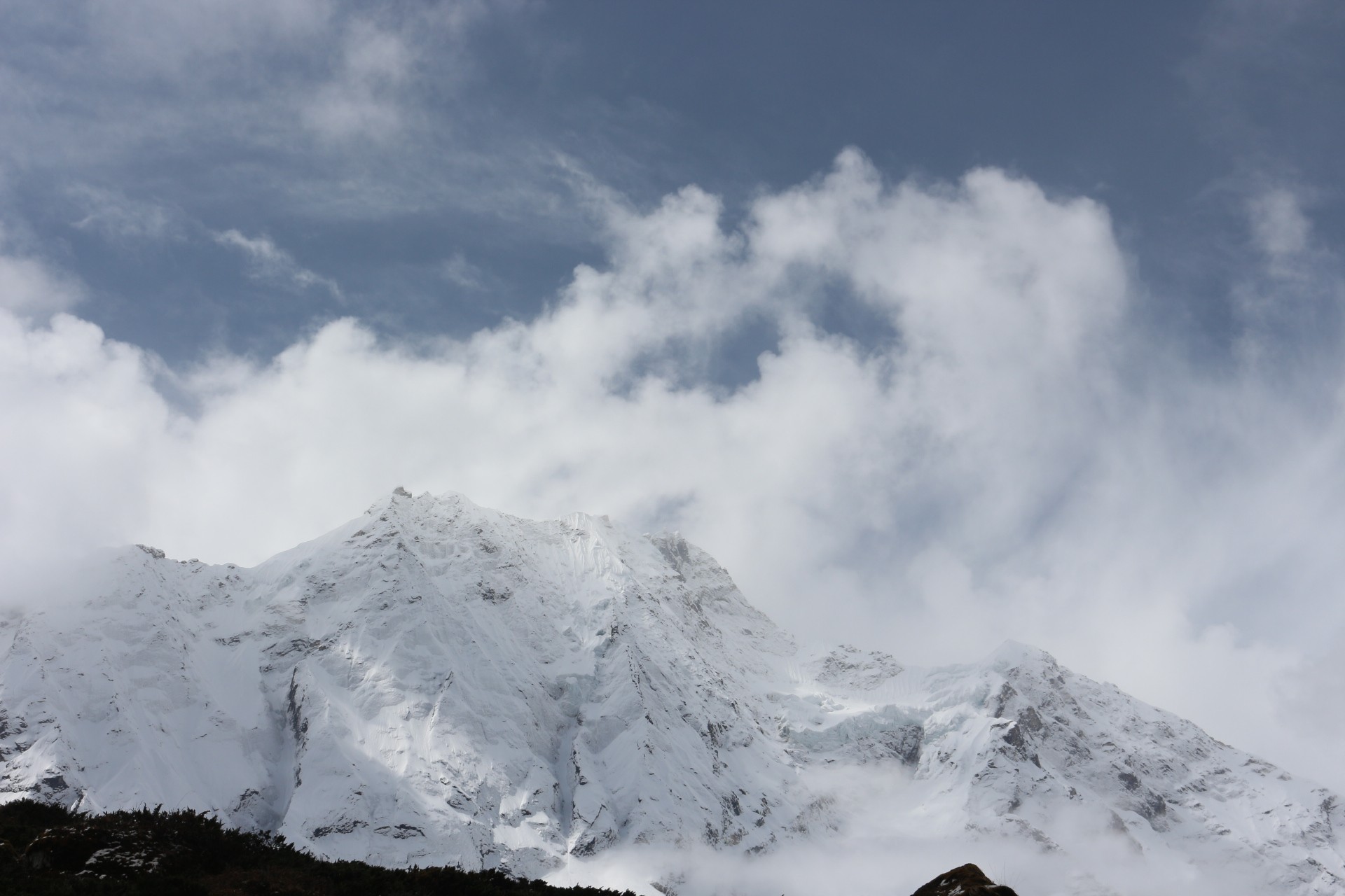  Snow-covered Himalayan peaks on the Manaslu Circuit Trek are partially wrapped in dramatic monsoon clouds, illustrating the changing September weather with fresh snowfall and mist drifting across the mountains.