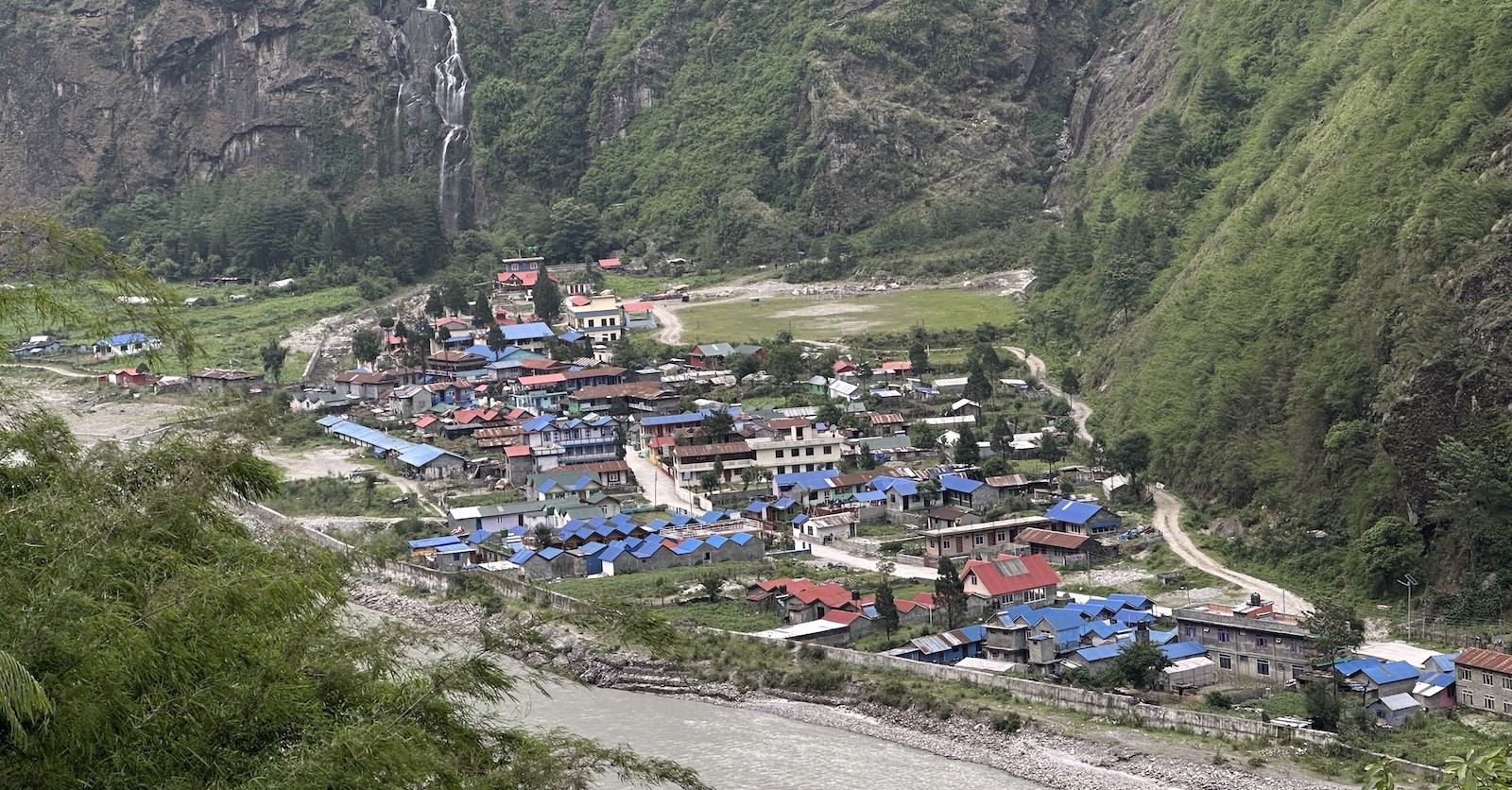 Scenic view of Tal along the Annapurna Circuit Trek, featuring traditional stone houses, waterfalls, a wide river valley, and surrounding Himalayan cliffs.