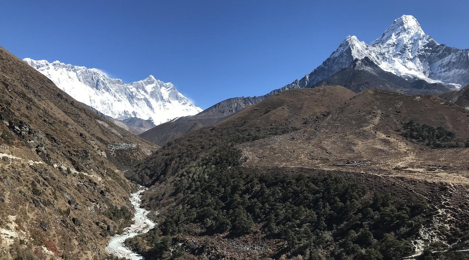 Trekking trail heading toward Dingboche through a wide Himalayan valley, with a flowing river, alpine meadows, and magnificent mountain views including Ama Dablam and surrounding Everest region peaks.