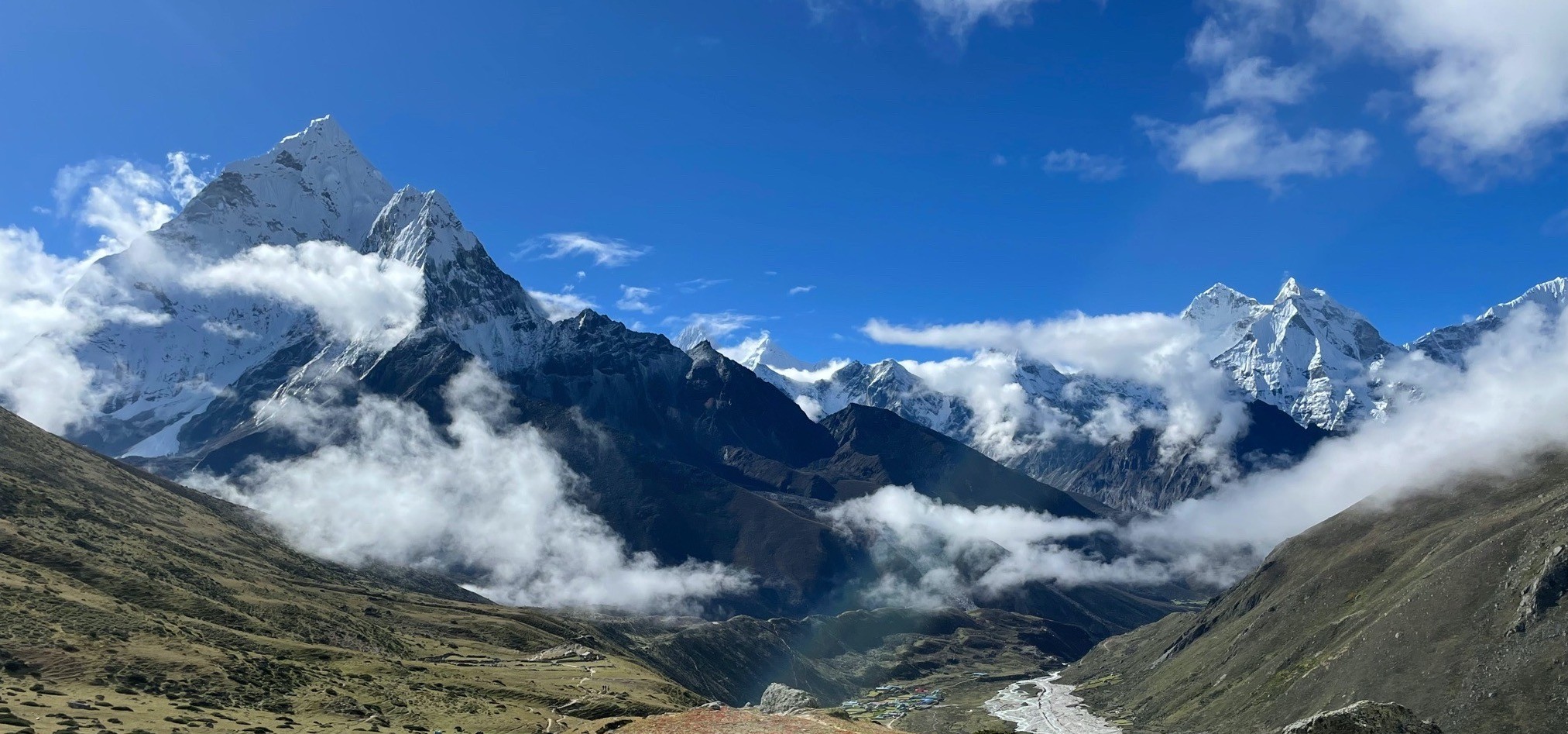 Panoramic view of Ama Dablam, and surrounding Everest region peaks rising above drifting clouds under a crystal-clear blue sky during the Everest Base Camp Trek.