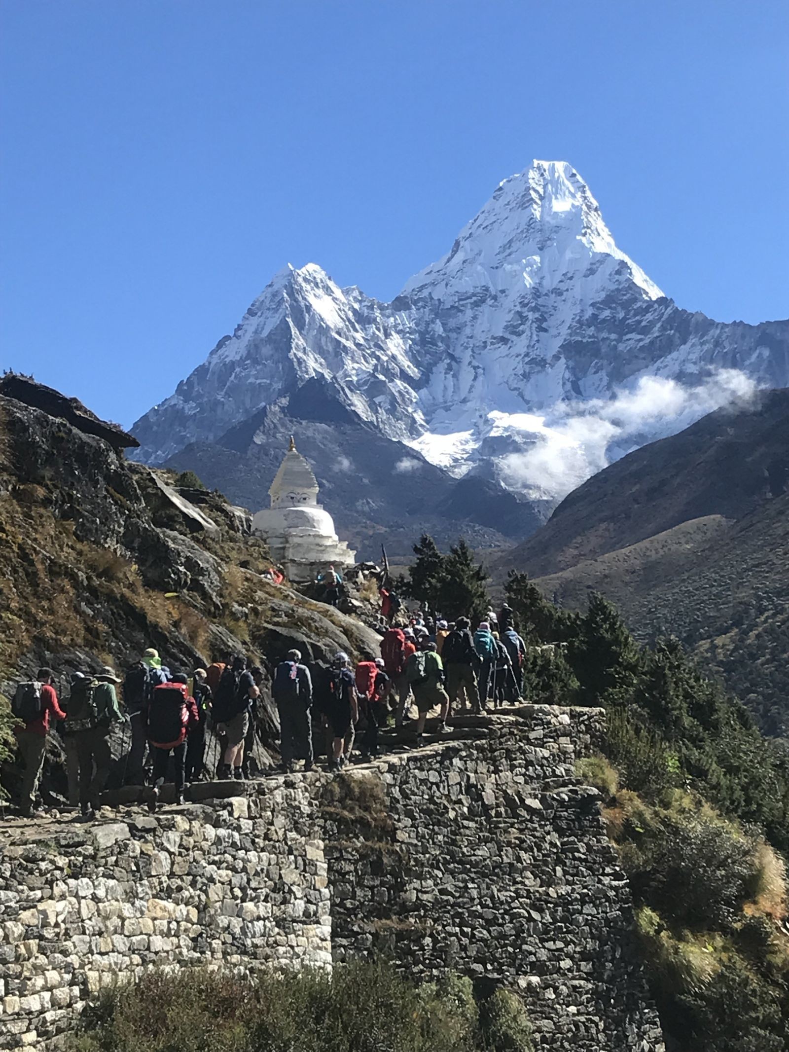 Trekkers hike along the alpine trail from Namche Bazaar to Dingboche with the iconic peak of Ama Dablam rising majestically above the Khumbu Valley beneath clear Himalayan skies.