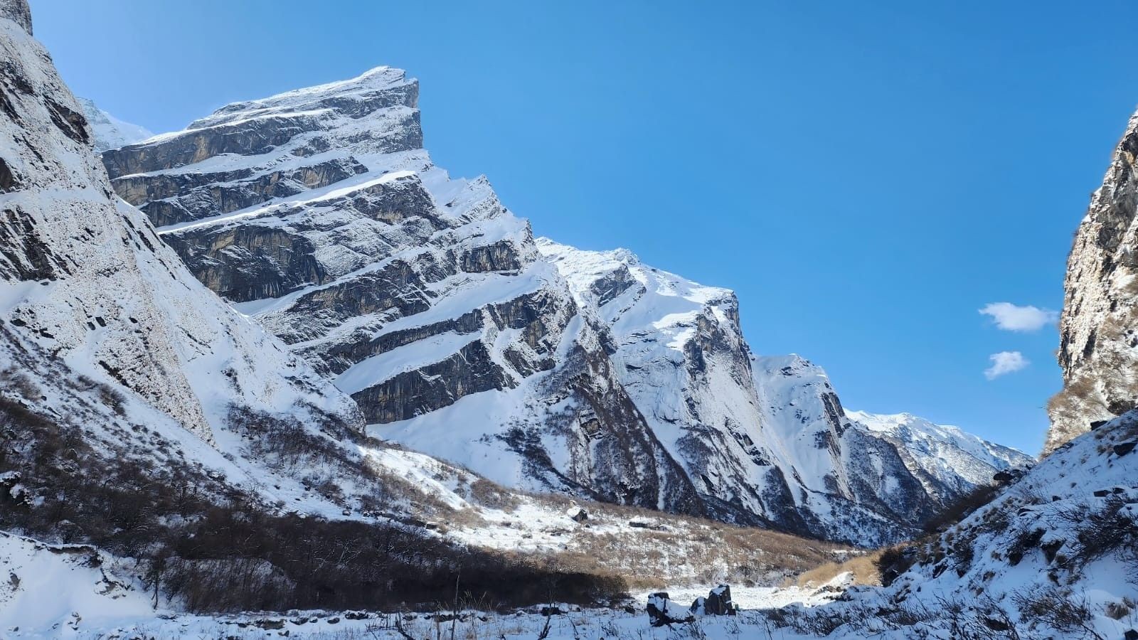 Snow-dusted Himalayan gorge along the Annapurna Base Camp Trek, featuring steep rocky cliffs, a narrow valley, and fresh snowfall.