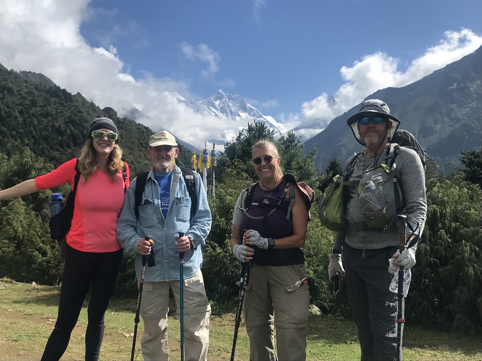 Trekker wearing comfortable day hiking clothes on the Everest Base Camp Trek in November, including thermal base layers, fleece jacket, waterproof shell, trekking pants, hiking boots, gloves, sunglasses, and a backpack with snow-capped Himalayan peaks in the background.