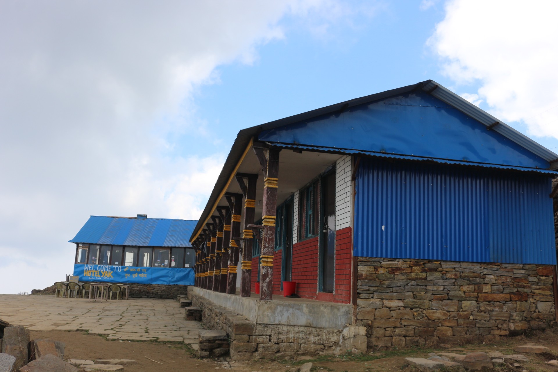 Traditional teahouse lodges at High Camp on the Mardi Himal Trek, featuring simple stone-and-metal buildings with blue roofs under a crisp October sky in Nepal's Annapurna region.