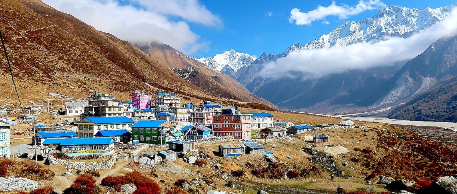 Traditional Kyanjin Gompa with nearby mountain lodges set against snow-capped Himalayan peaks in Langtang Valley, Nepal.