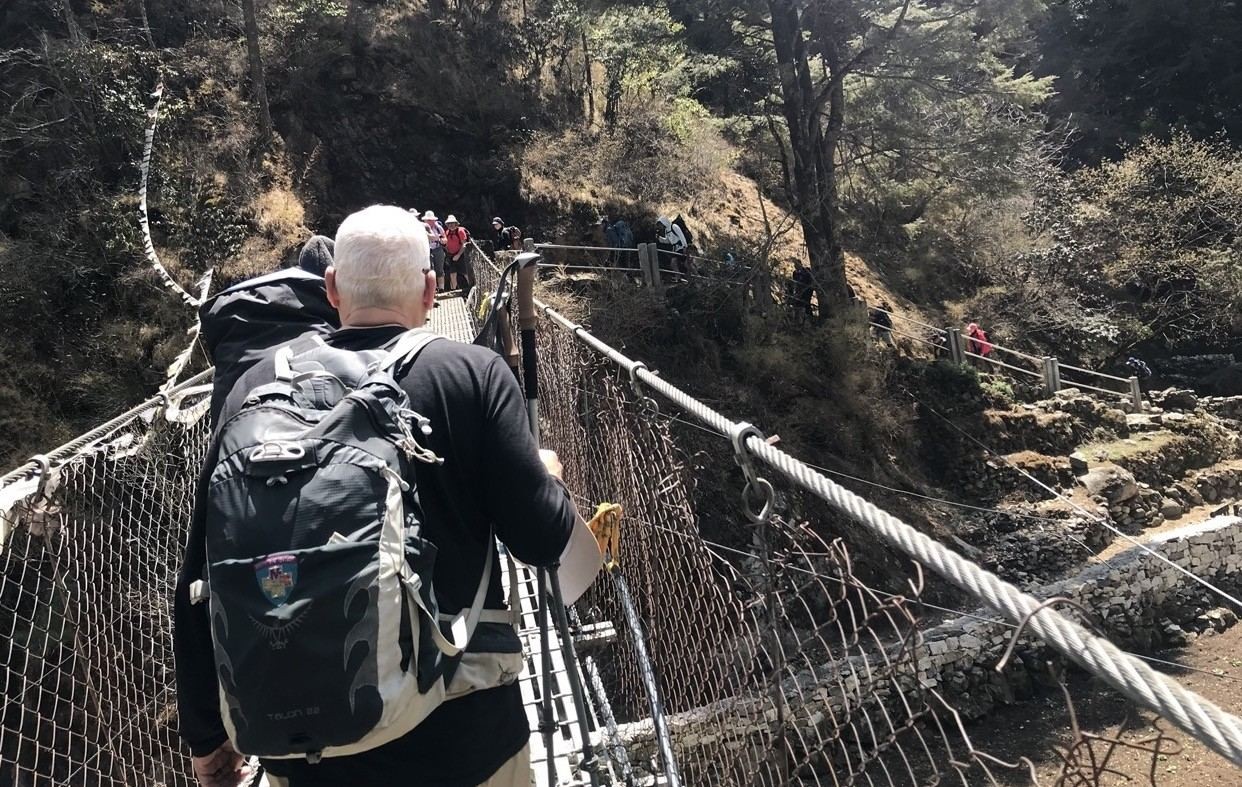 Busy Himalayan trekking trail in Nepal with groups of trekkers creating congestion on narrow paths, suspension bridges, and mountain routes during peak season.