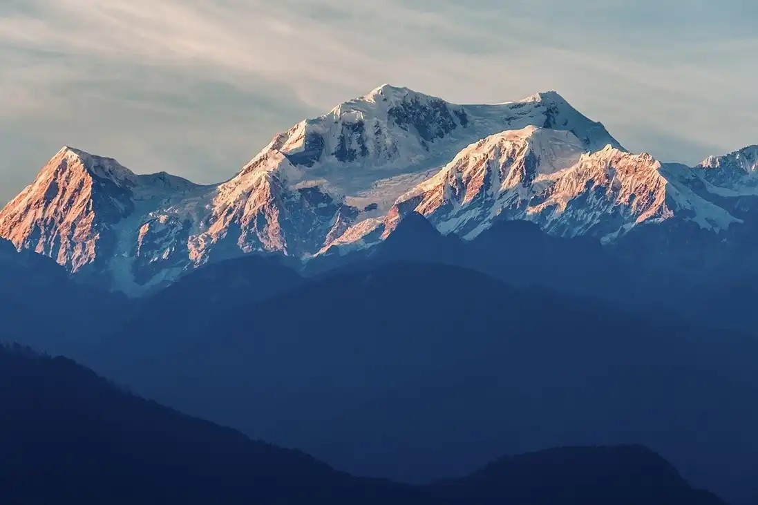 Majestic view of Kangchenjunga with its snow-covered peaks rising above remote Himalayan valleys and clouds in eastern Nepal.