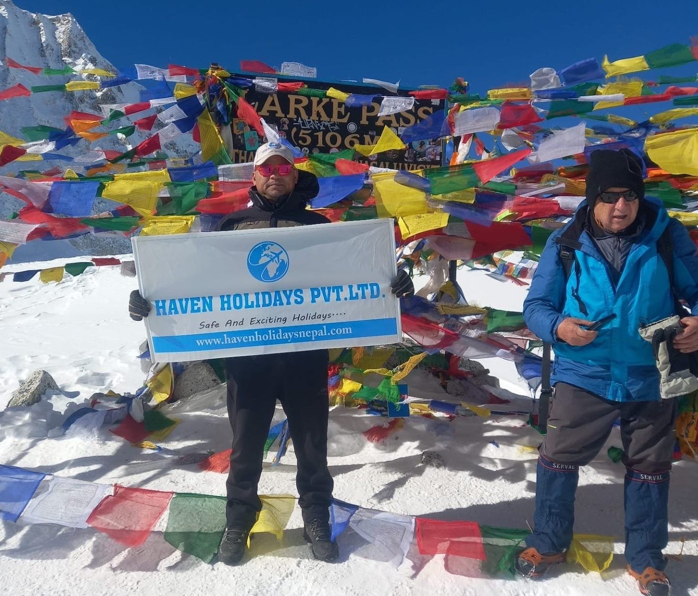 Trekker at Larke Pass (5,106 m) on the Manaslu Circuit Trek with colorful prayer flags and snowy Himalayan peaks.