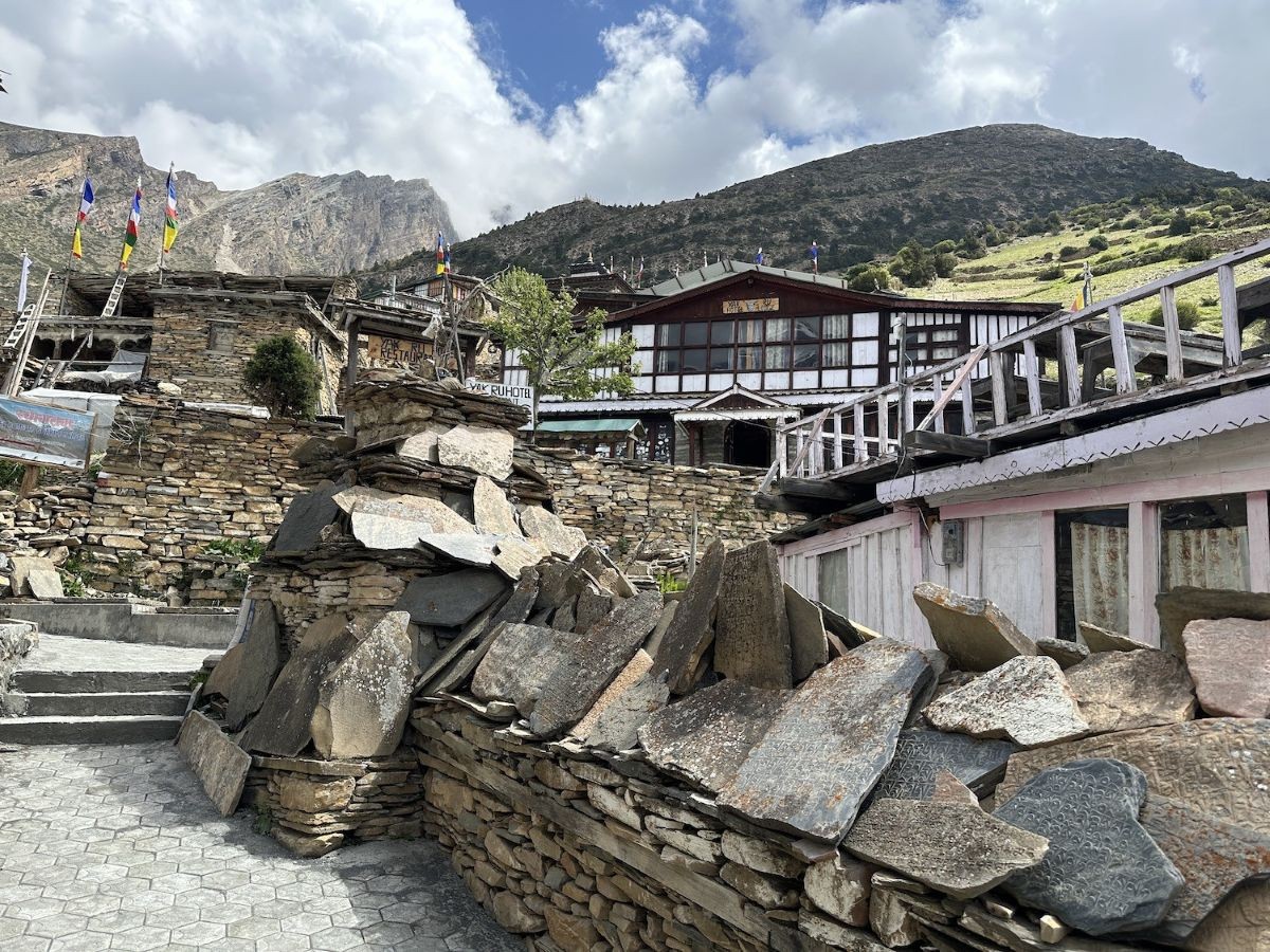 Traditional stone houses in Ghyaru Village on the Annapurna Circuit Trek with ancient mani walls, colorful prayer flags, terraced hillsides, and spectacular views of Annapurna II, Annapurna III, Annapurna IV, and Gangapurna in Nepal.