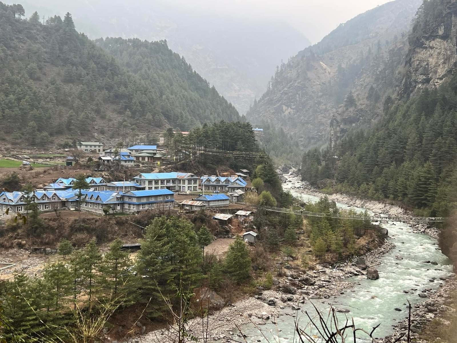 Scenic view of Phakding featuring traditional teahouses, colorful lodges, the Dudh Koshi River, suspension bridges, and forested Himalayan landscapes along the Everest Base Camp Trek route.