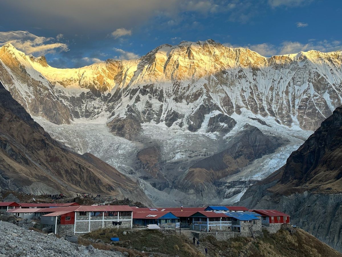 Golden sunrise illuminating Annapurna I above Annapurna Base Camp, with glaciers, colorful teahouses, and trekkers enjoying spectacular Himalayan views in Nepal.