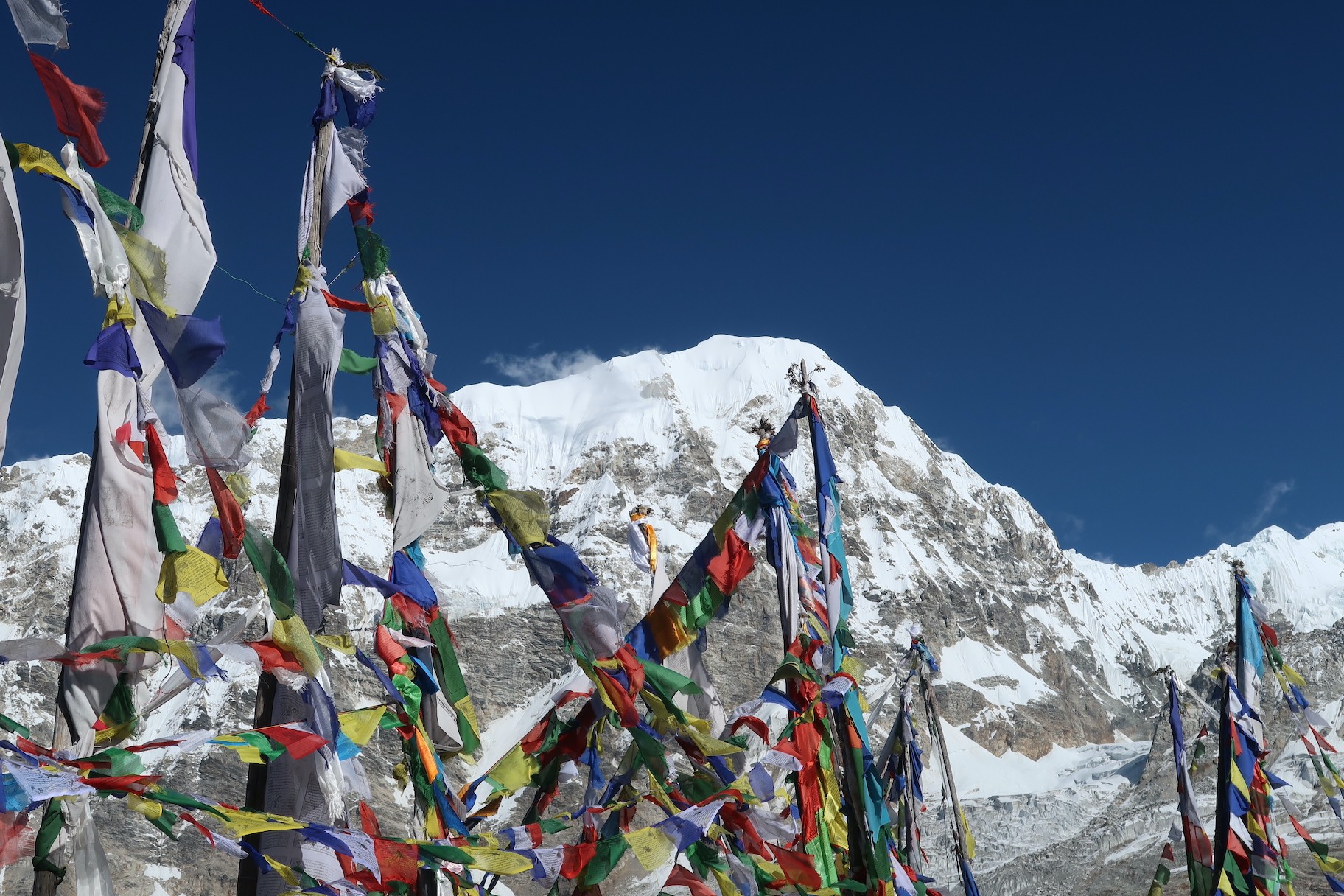 Colorful prayer flags fluttering on Tserko Ri summit in October with panoramic views of Langtang Lirung, snow-covered Himalayan peaks, glaciers, and crystal-clear blue skies in Langtang National Park, Nepal.