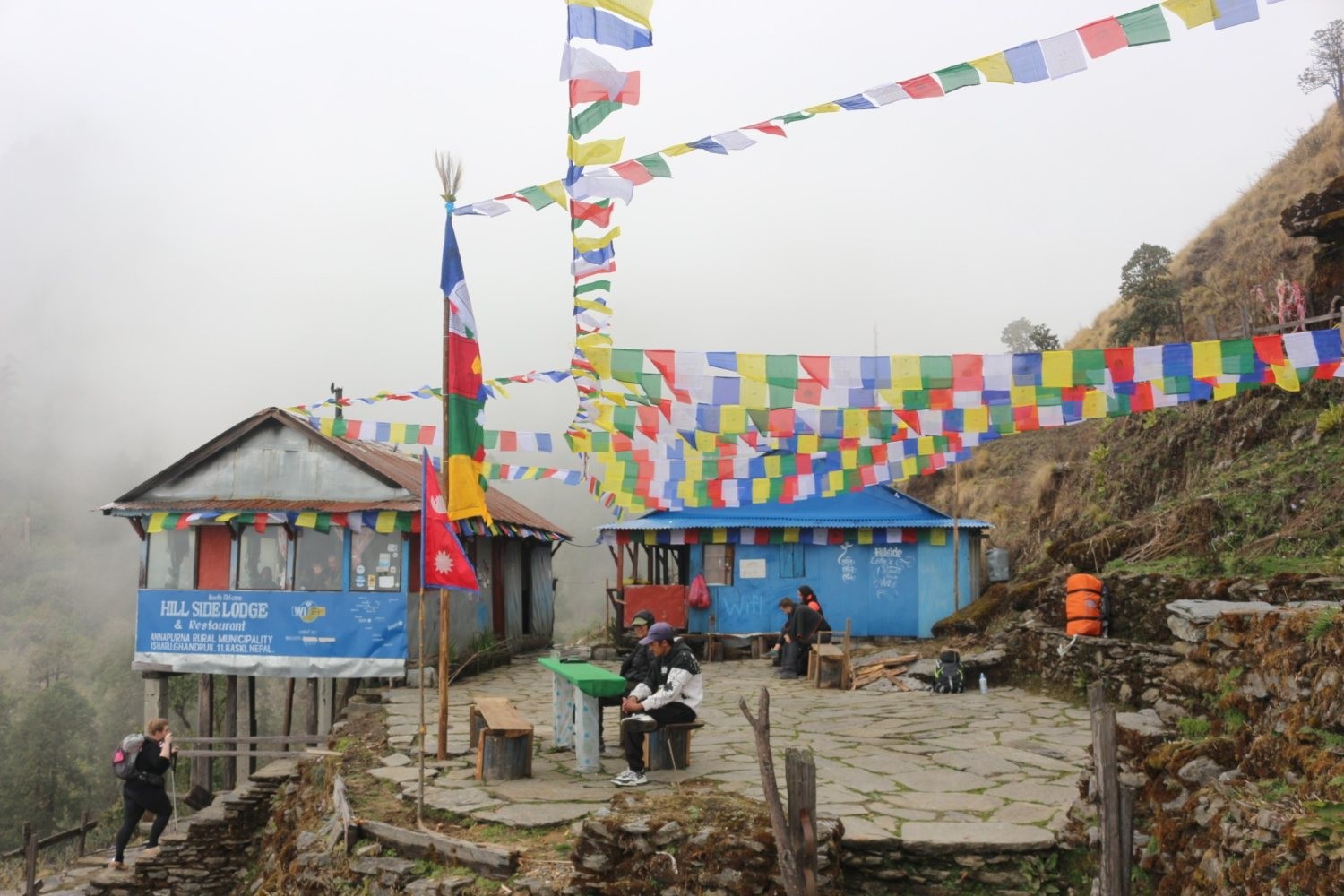 Trekkers hiking on a rugged mountain trail with changing weather conditions, showcasing high-altitude landscapes, rocky paths, and panoramic Himalayan views on the Muldai Hill Trek in Nepal.