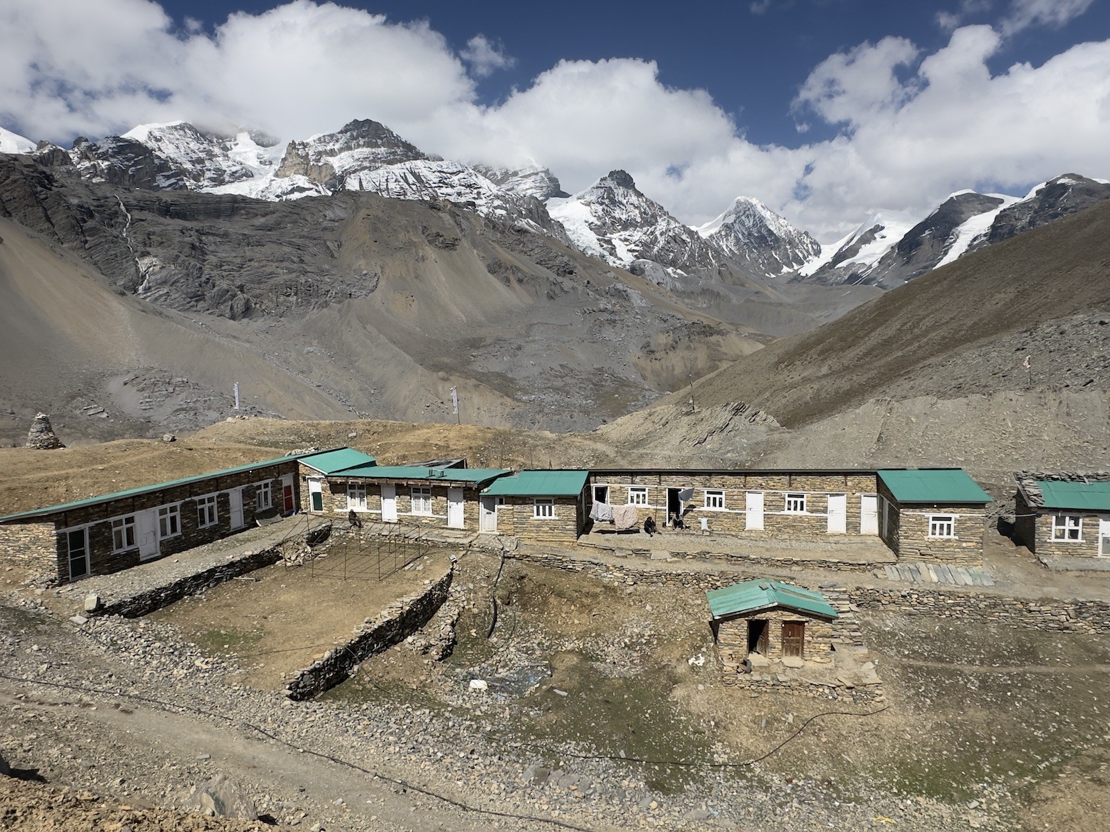 Thorong High Camp with traditional mountain lodges, trekkers preparing for the ascent to Thorong La Pass, surrounded by rugged alpine terrain and snow-covered Himalayan peaks in Nepal.