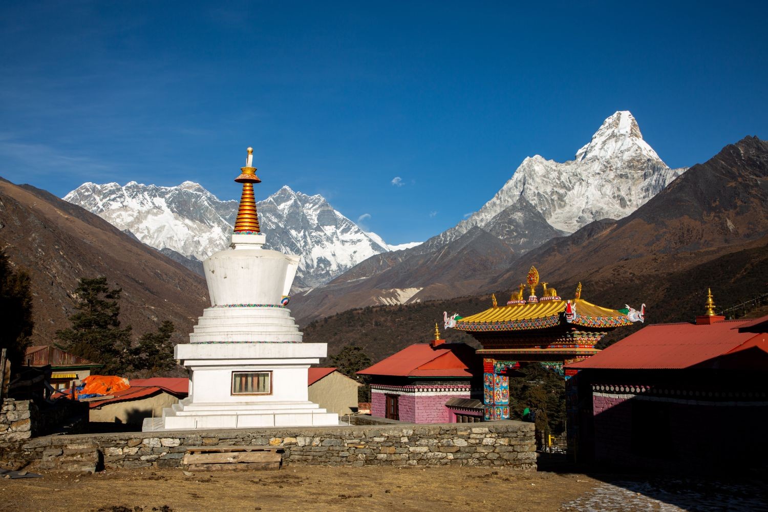 "Tengboche Monastery surrounded by snow-capped Himalayan peaks, colourful prayer flags, and towering pine forests on the Everest Base Camp Trek in Nepal"