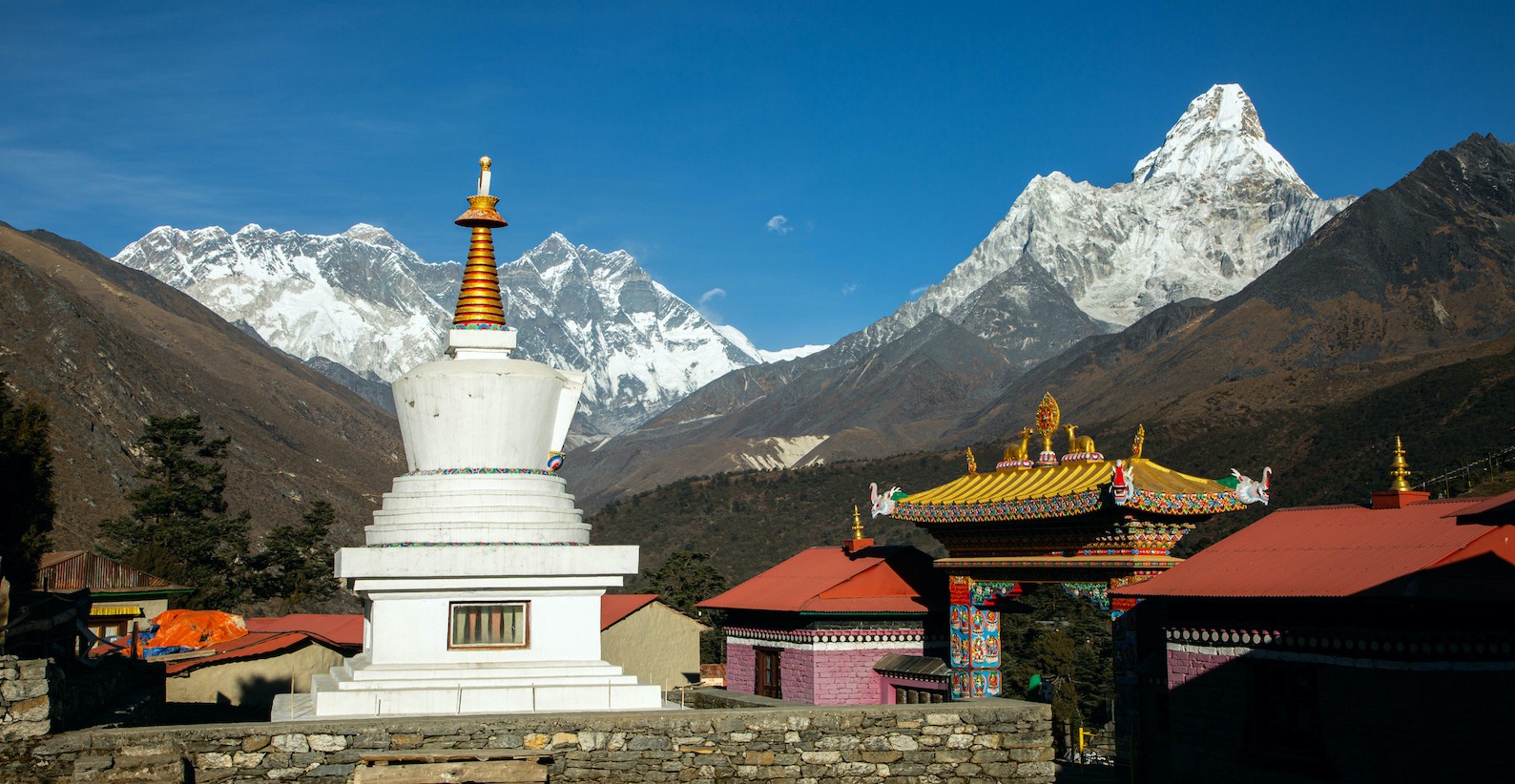 Tengboche Monastery surrounded by dramatic Himalayan mountain views, including Ama Dablam and Everest region peaks, with prayer flags and alpine landscape.