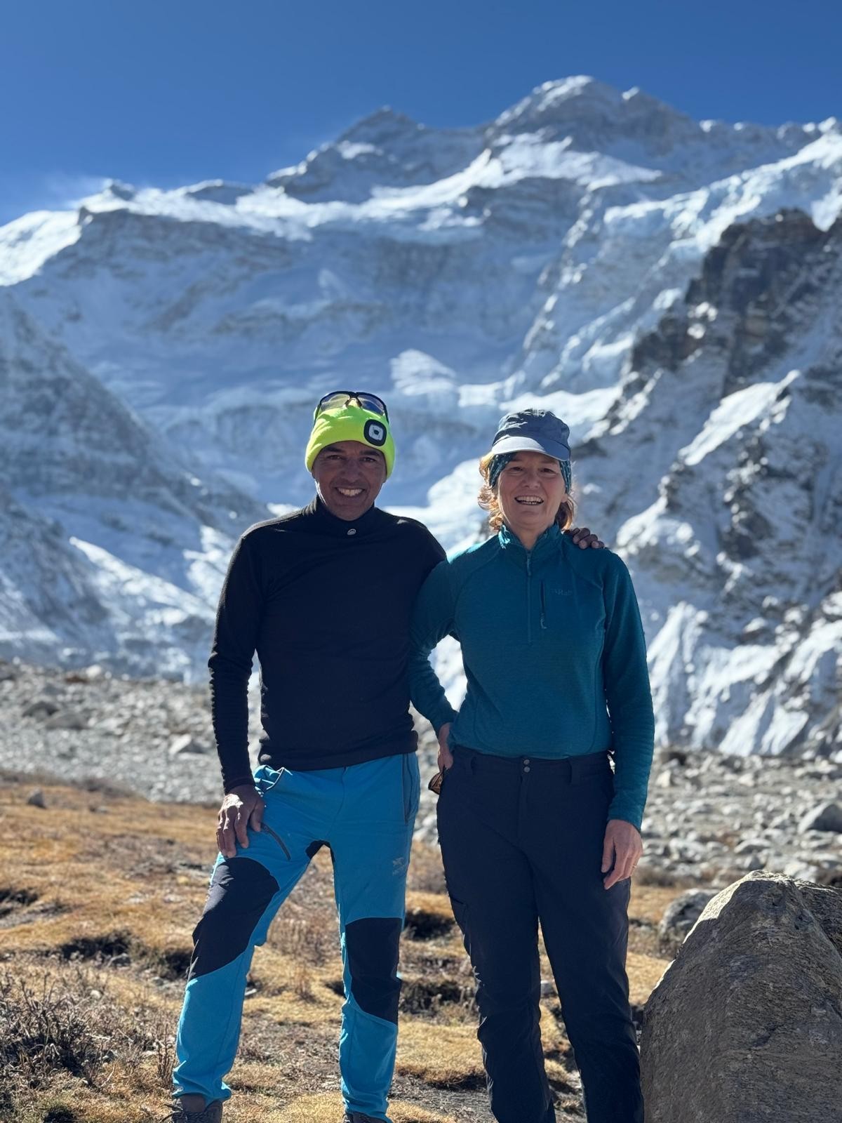 Trekkers standing at Kanchenjunga Base Camp surrounded by breath-taking Himalayan peaks under a clear blue sky, enjoying stunning mountain views and perfect trekking weather.