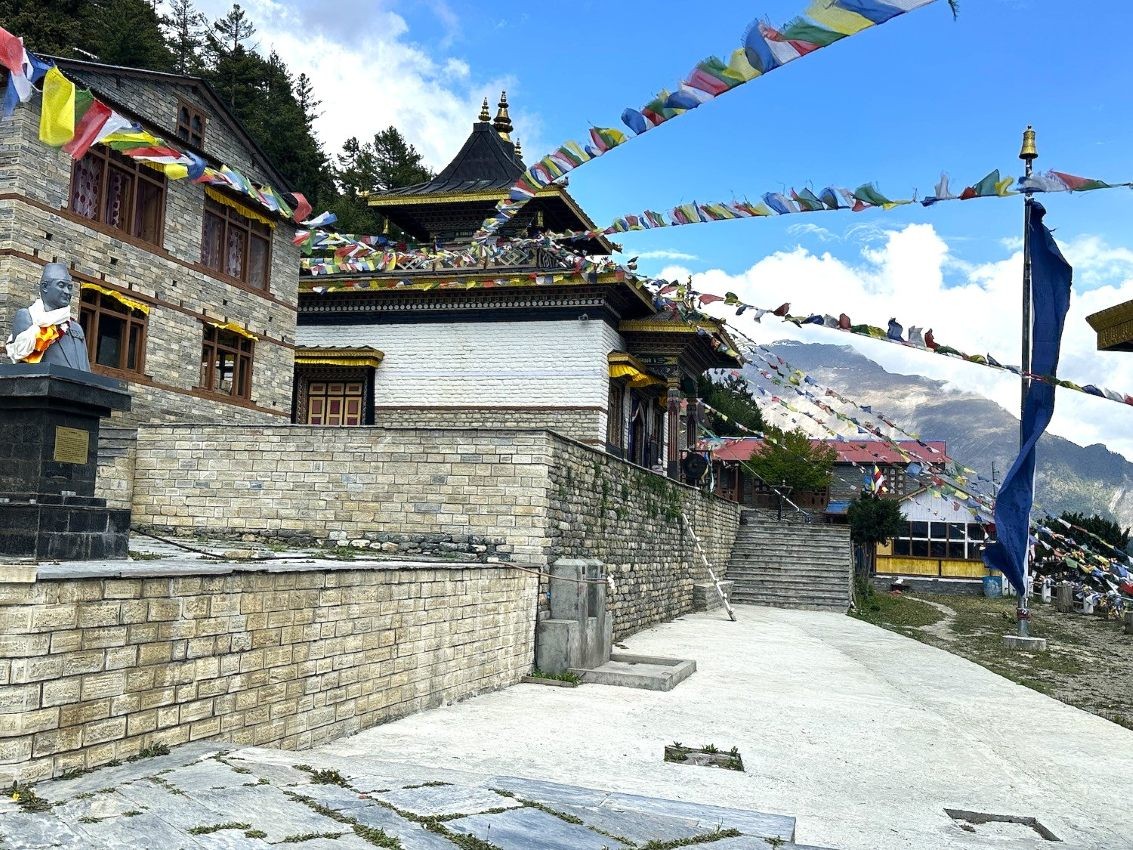 Ancient Pisang Monastery in Upper Pisang on the Annapurna Circuit Trek, featuring traditional Tibetan Buddhist architecture, colorful prayer flags, mani walls, and stunning views of Annapurna II and the surrounding Himalayan mountains.