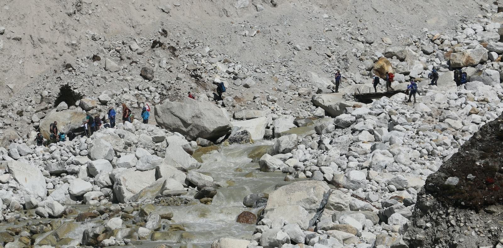 Narrow and steep Himalayan trekking trail in Nepal with loose stones and trekkers carefully navigating a bottleneck section on rugged mountain terrain.