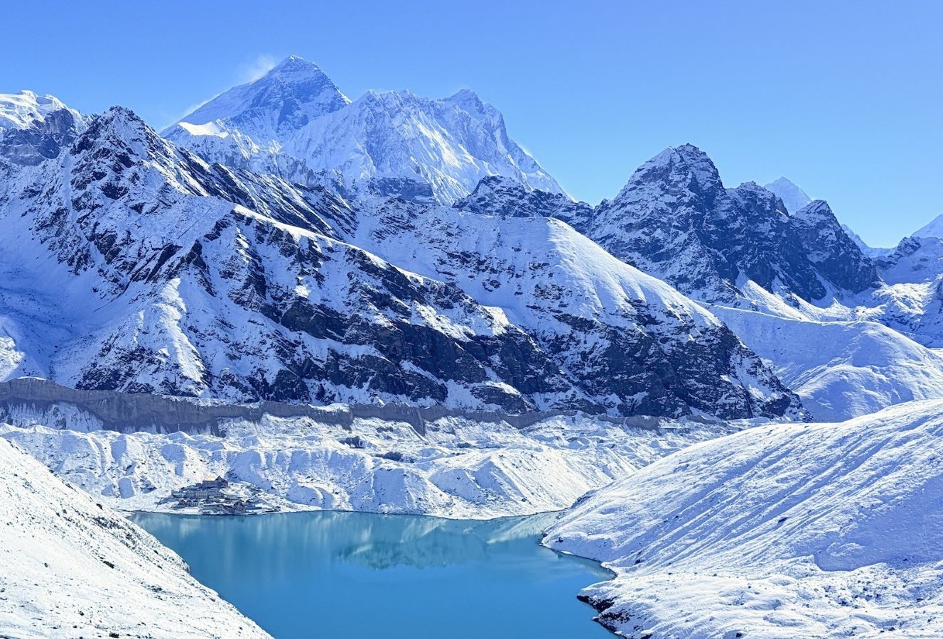 Gokyo Ri summit climb in winter with trekkers standing on a snowy viewpoint overlooking frozen Gokyo Lakes and panoramic Himalayan peaks 