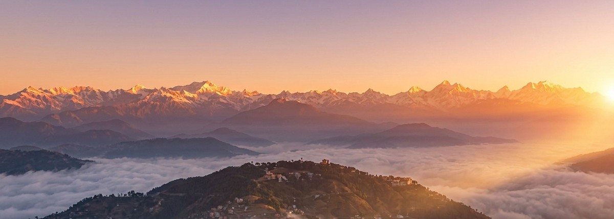 Sunrise view from Nagarkot with the Himalayan range glowing in golden light above rolling green hills and mist-filled valleys near Kathmandu, Nepal.