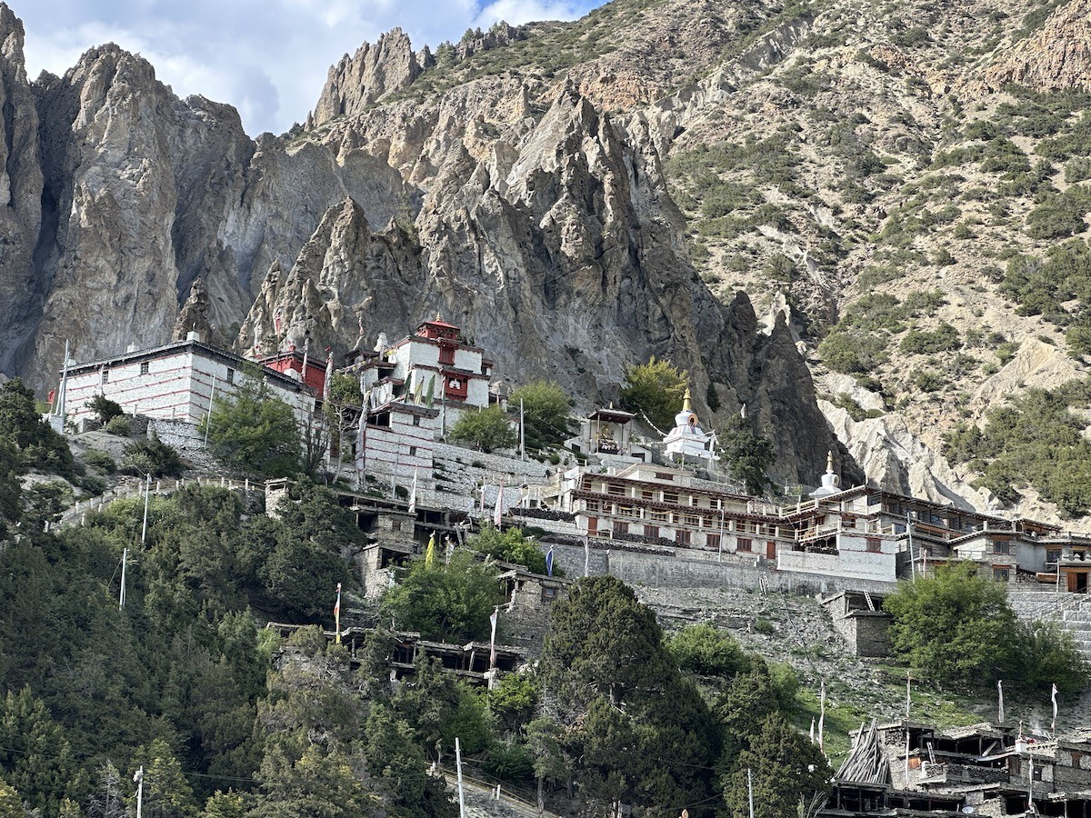 Traditional Braga Village with ancient stone houses, Braga Monastery, colorful prayer flags, and panoramic views of the Annapurna Himalayas near Manang on the Annapurna Circuit Trek in Nepal.