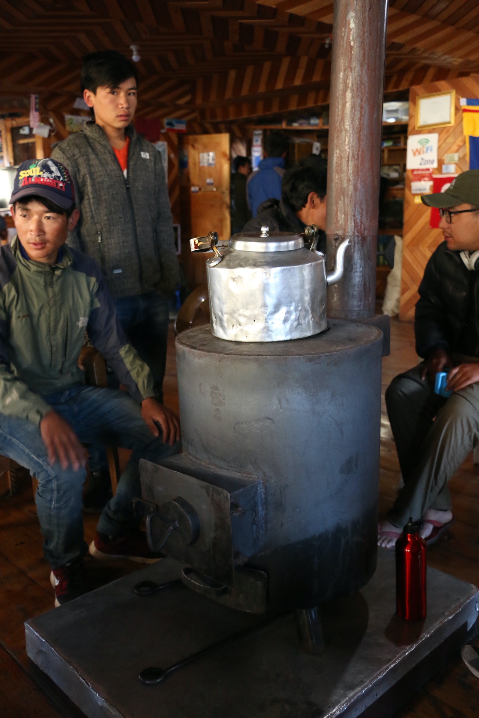 Trekkers gathering around a traditional wood-burning stove inside a mountain teahouse in Nepal, staying warm after sunset during a chilly October trek in the Himalayas.