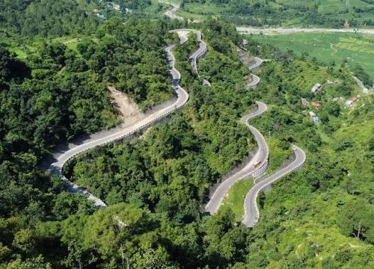 "BP Highway winding through lush green hills with sharp hairpin bends, connecting Kathmandu to eastern Nepal on the route toward the Everest region."