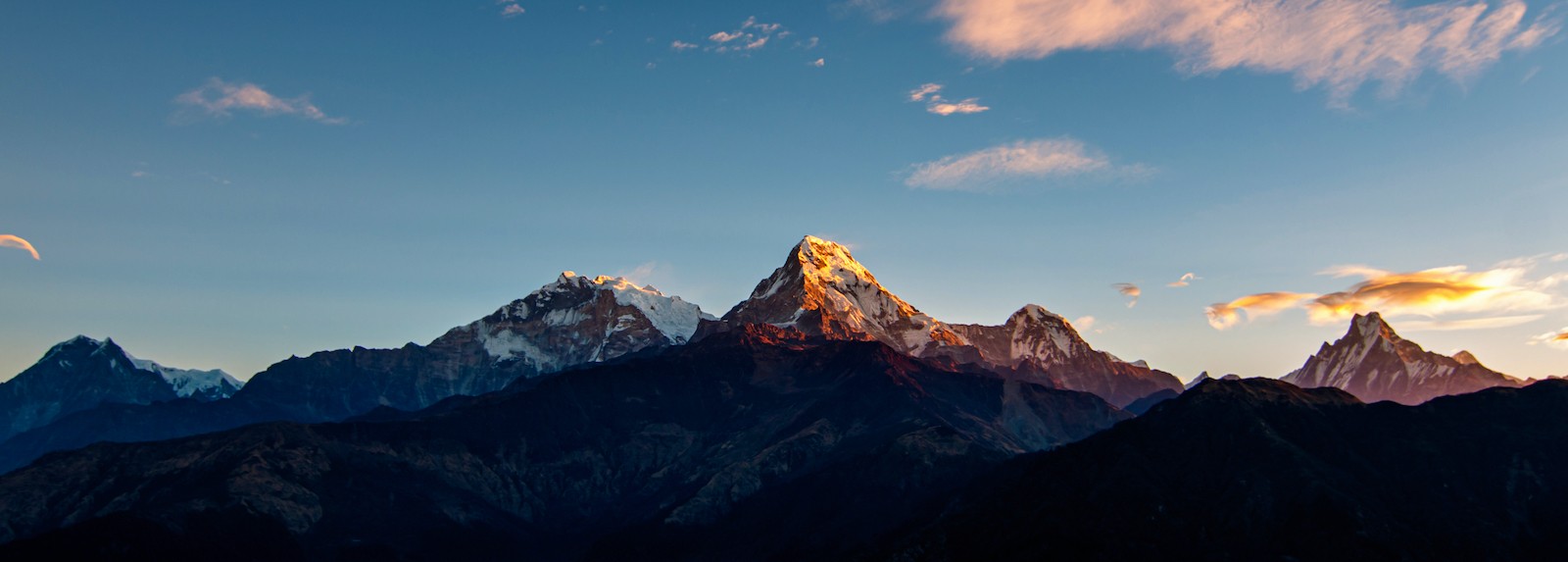 Golden sunrise over Annapurna South, Hiunchuli, and Machhapuchhre (Fishtail) viewed from Poon Hill, with snow-capped Himalayan peaks glowing against a colorful morning sky.
