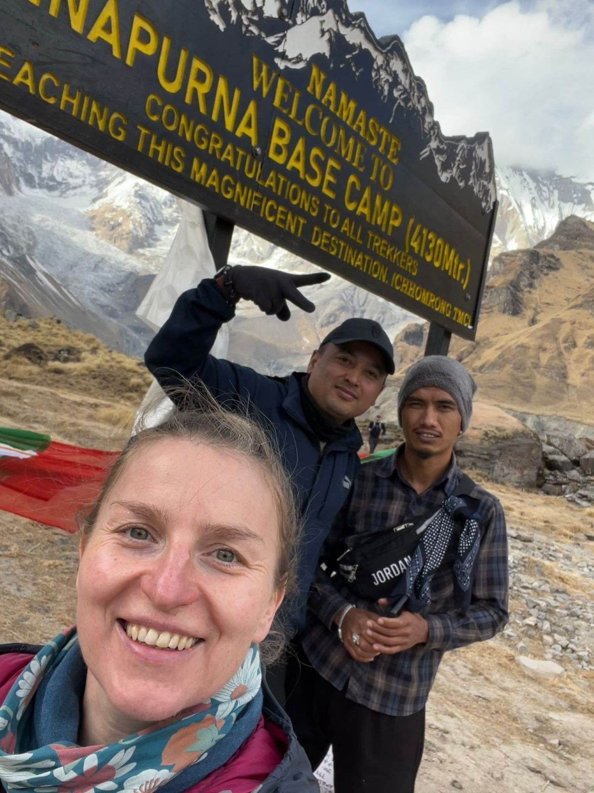 Trekkers posing beside the Annapurna Base Camp signboard at 4,130 meters, surrounded by the majestic snow-covered peaks of the Annapurna Sanctuary in Nepal.