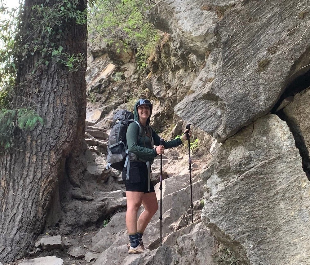 Solo female trekker hiking on a rocky mountain trail in Nepal with a backpack and trekking poles during a safe Himalayan trekking adventure.