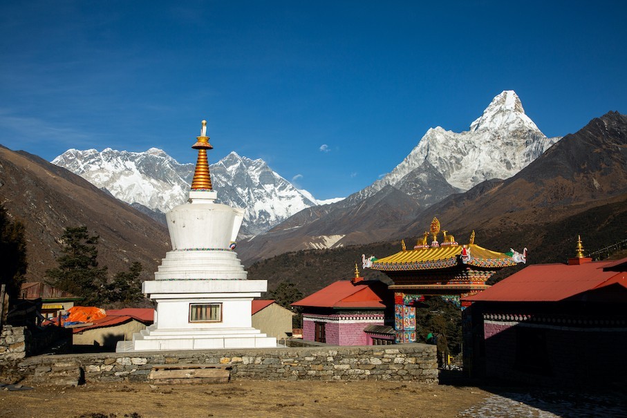 "Tengboche Monastery with a white Buddhist stupa and the snow-capped peaks of Ama Dablam, Everest, and Lhotse rising under a clear blue Himalayan sky."