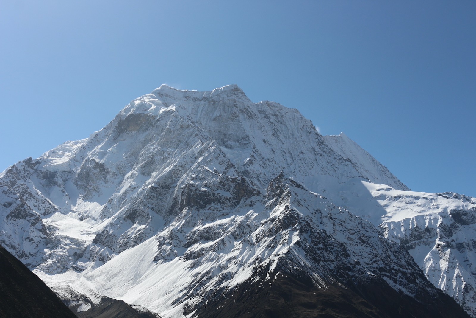 A majestic snow-covered Himalayan peak on the Manaslu Circuit Trek stands beneath a crystal-clear blue September sky, showcasing excellent visibility, glaciers, and rugged alpine ridges after the monsoon season.