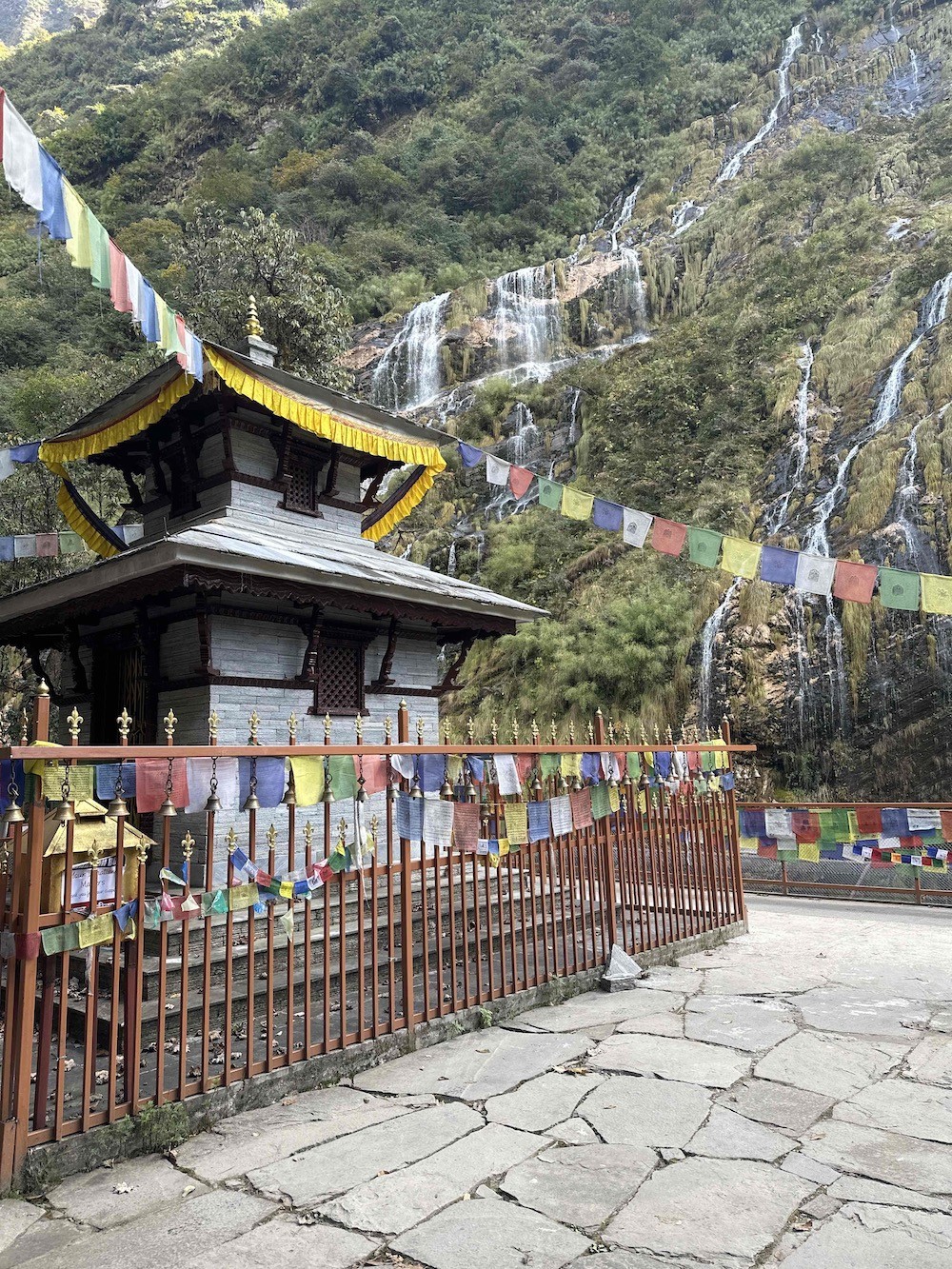 Traditional Baraha temple with colourful prayer flags and cascading waterfalls on the Annapurna Base Camp Trek
