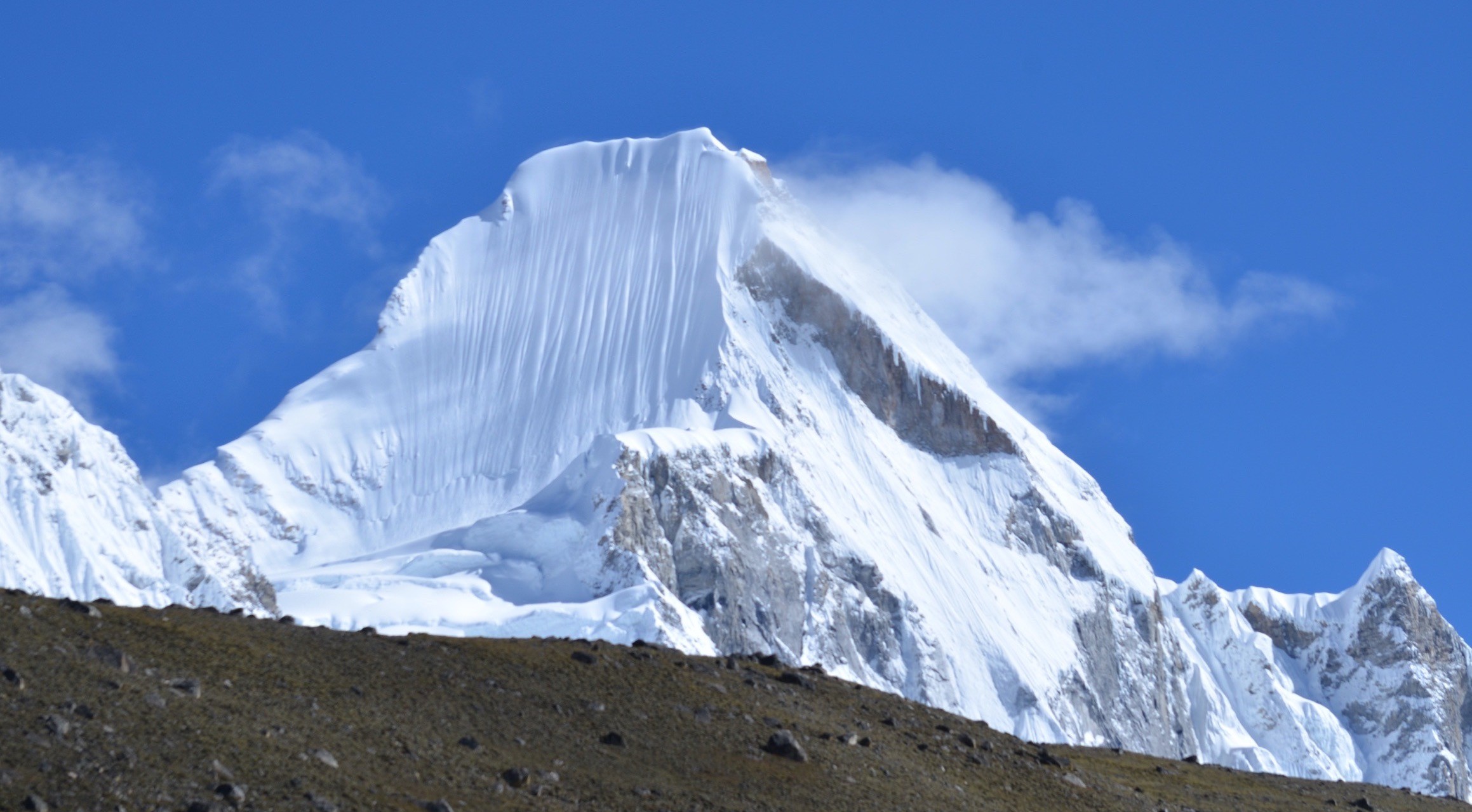 Crystal-clear blue sky above a spectacular snow-covered Himalayan peak with dramatic ice formations, offering exceptional visibility for mountain photography during autumn trekking in Nepal.